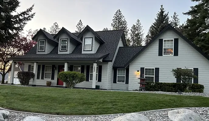 Two-story Spokane home after exterior house painting, with pale grey siding, black shutters and a freshly finished covered porch