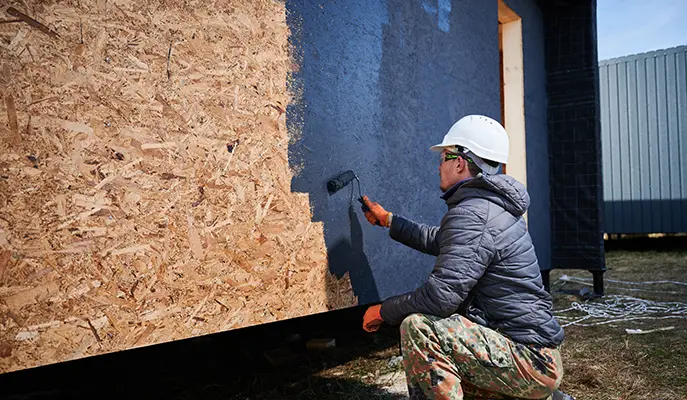 painter applying primer to the exterior of a house