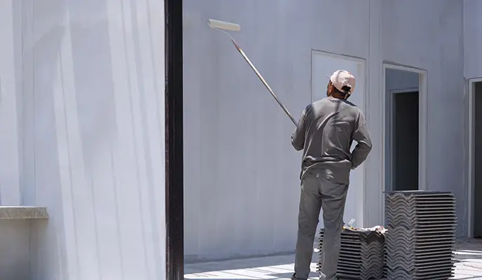 a painter in a gray uniform is painting the exterior of a house