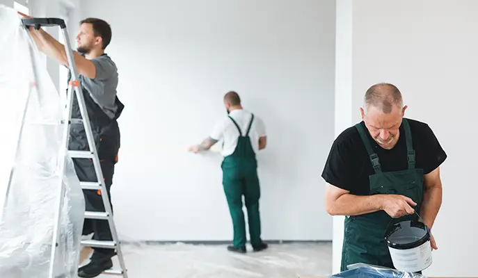 Three workers paint the inside of a house