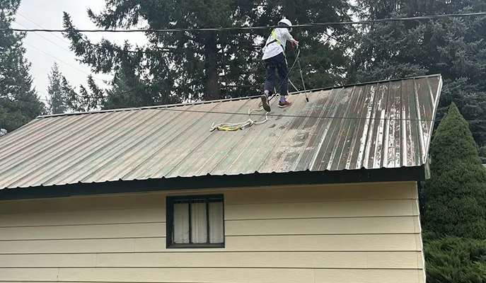 A painter removes rust from a roof before painting